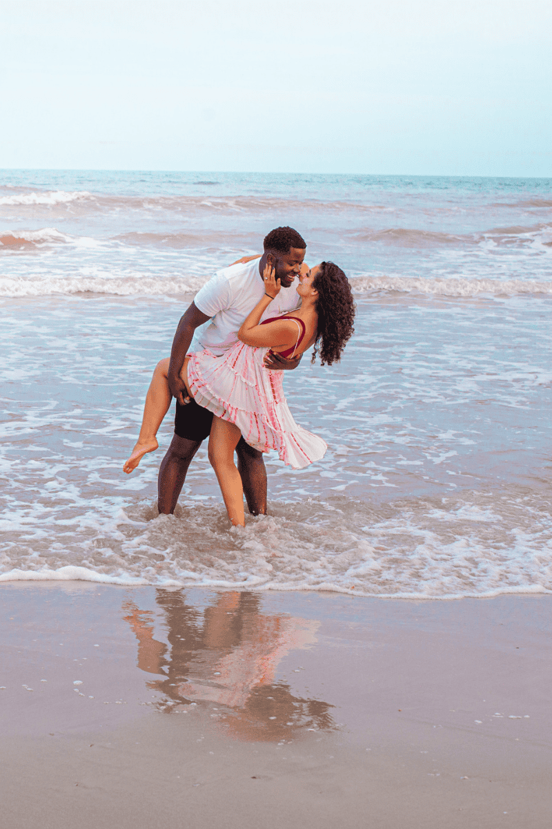 A couple embracing on the beach with waves around their feet.