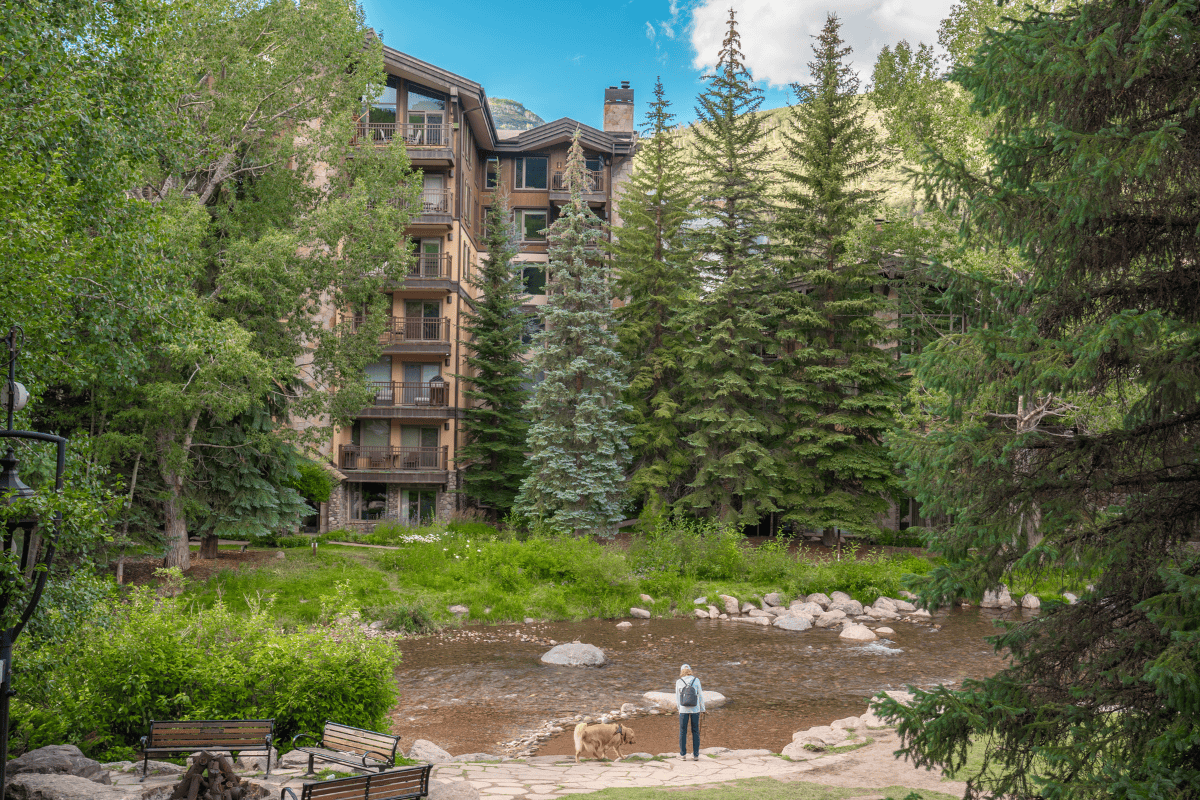 A person stands by a creek in front of a multi-story building