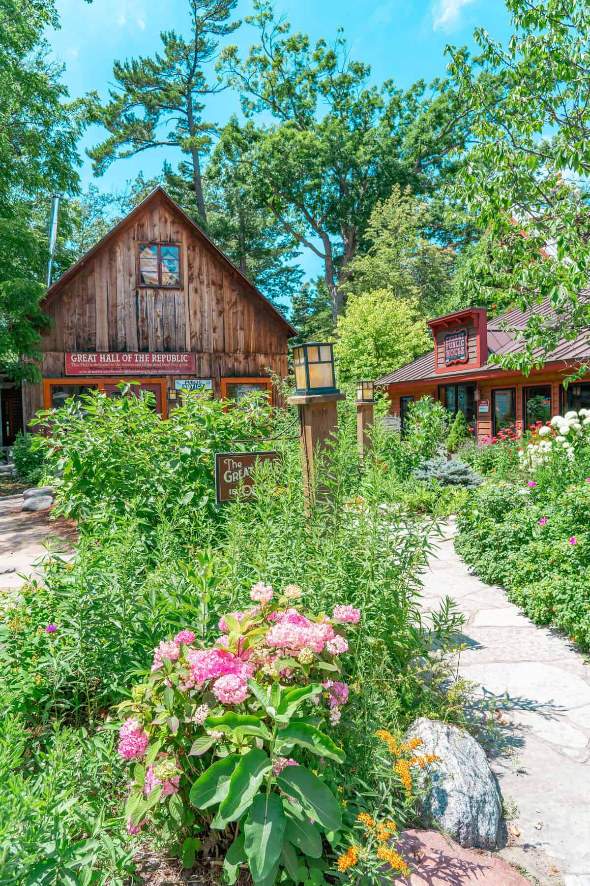 Rustic wooden buildings surrounded by lush garden and clear blue sky.