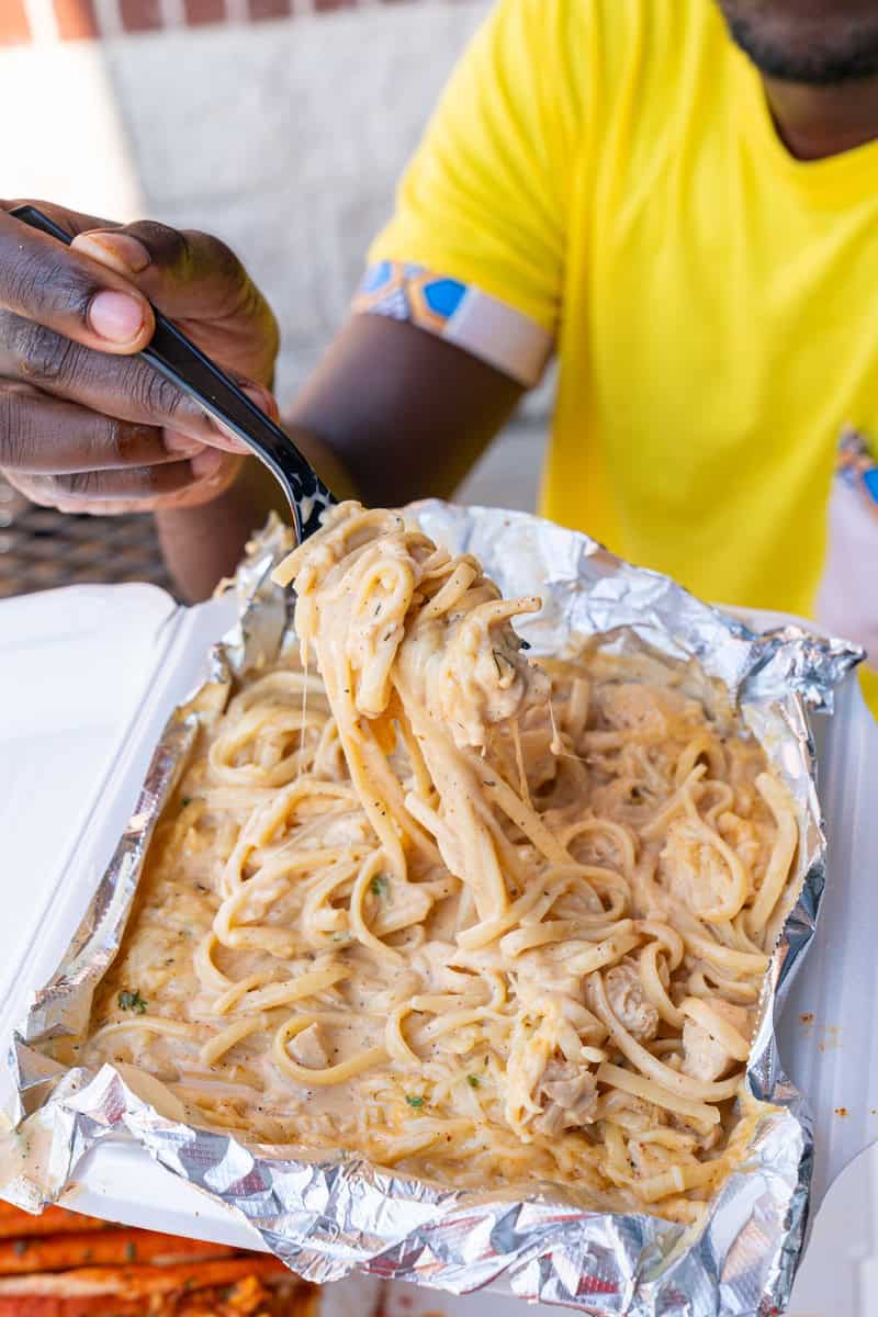 Person eating creamy pasta from a foil container with a fork.