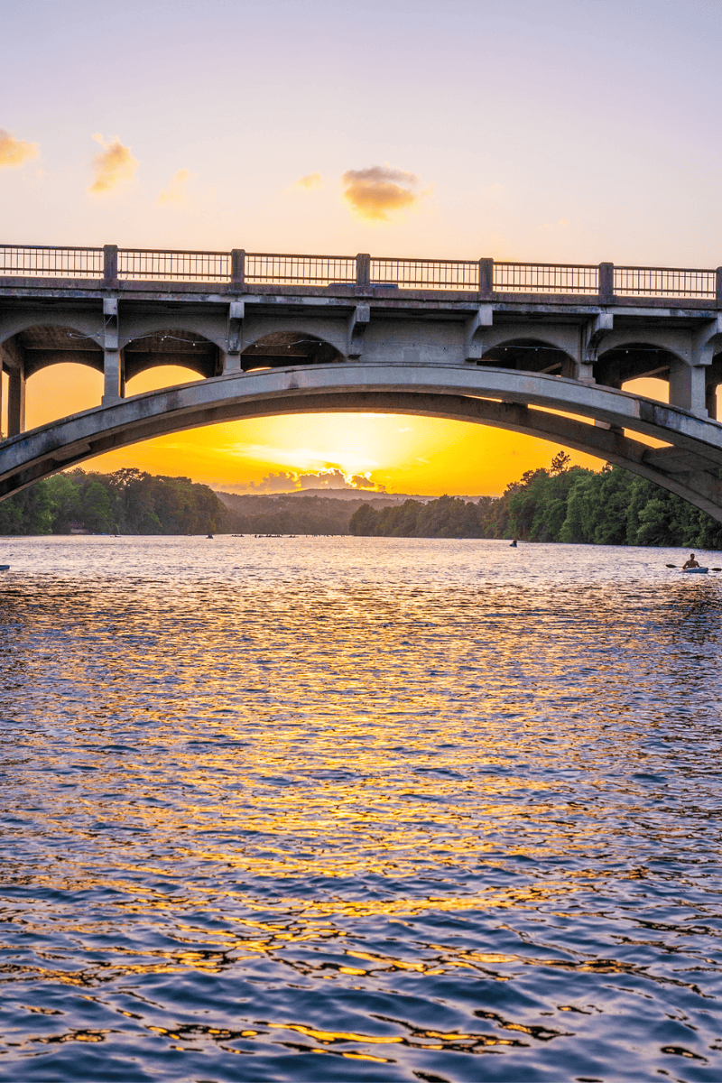 Sunset behind an arch bridge reflecting on water.