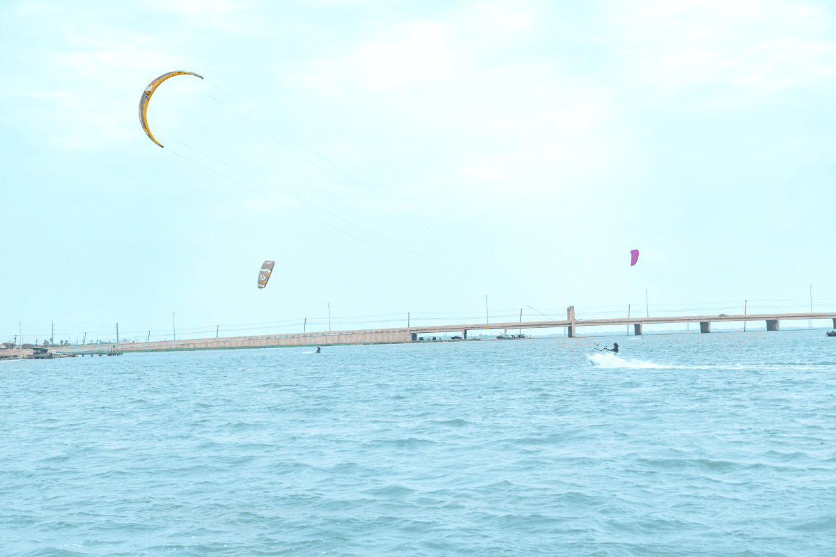 Kite surfers on choppy water with a bridge in the background.