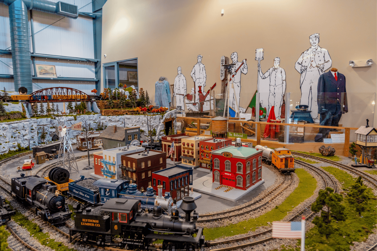 A detailed model train setup with tracks, miniature buildings, and trains in a room.