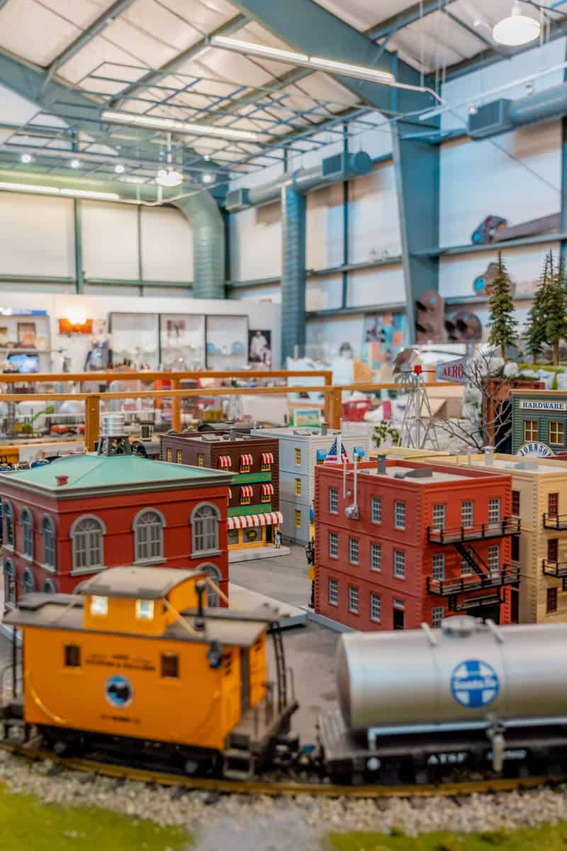 Detailed model train setup with buildings and a yellow caboose in the foreground.