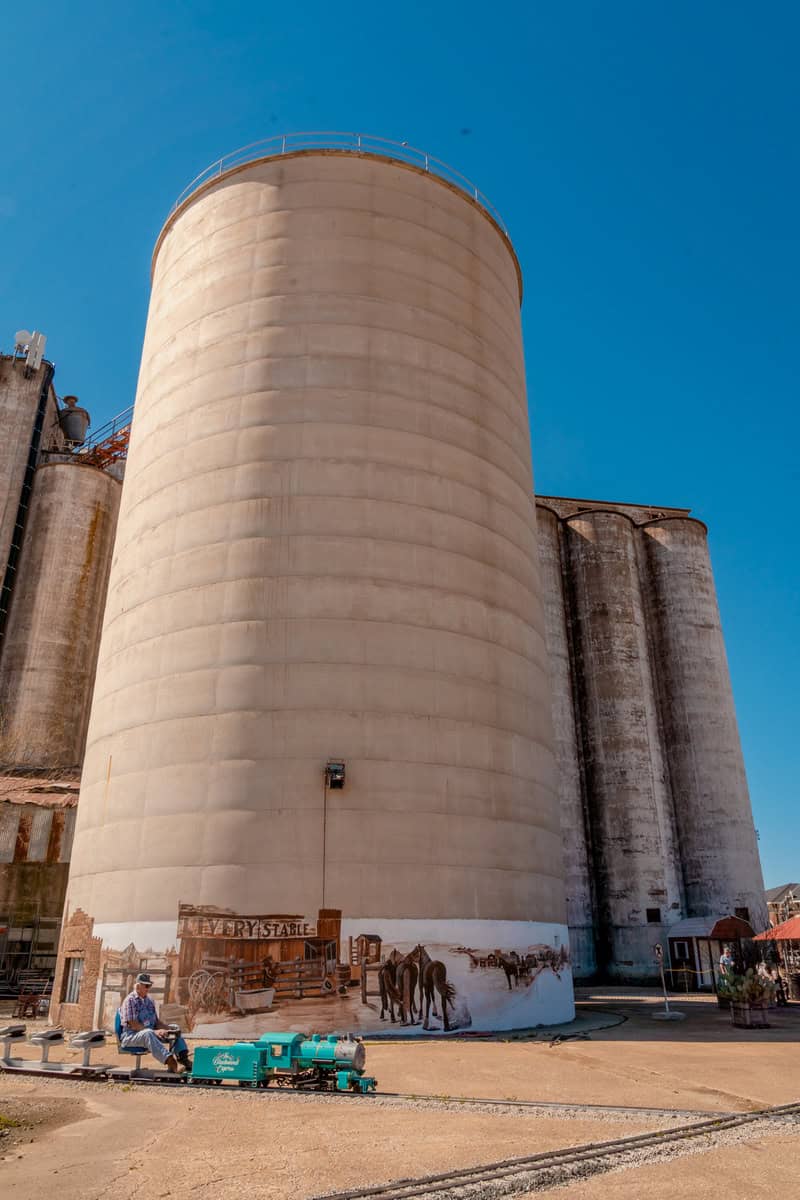 Large industrial silos with mural and man on toy train in front.