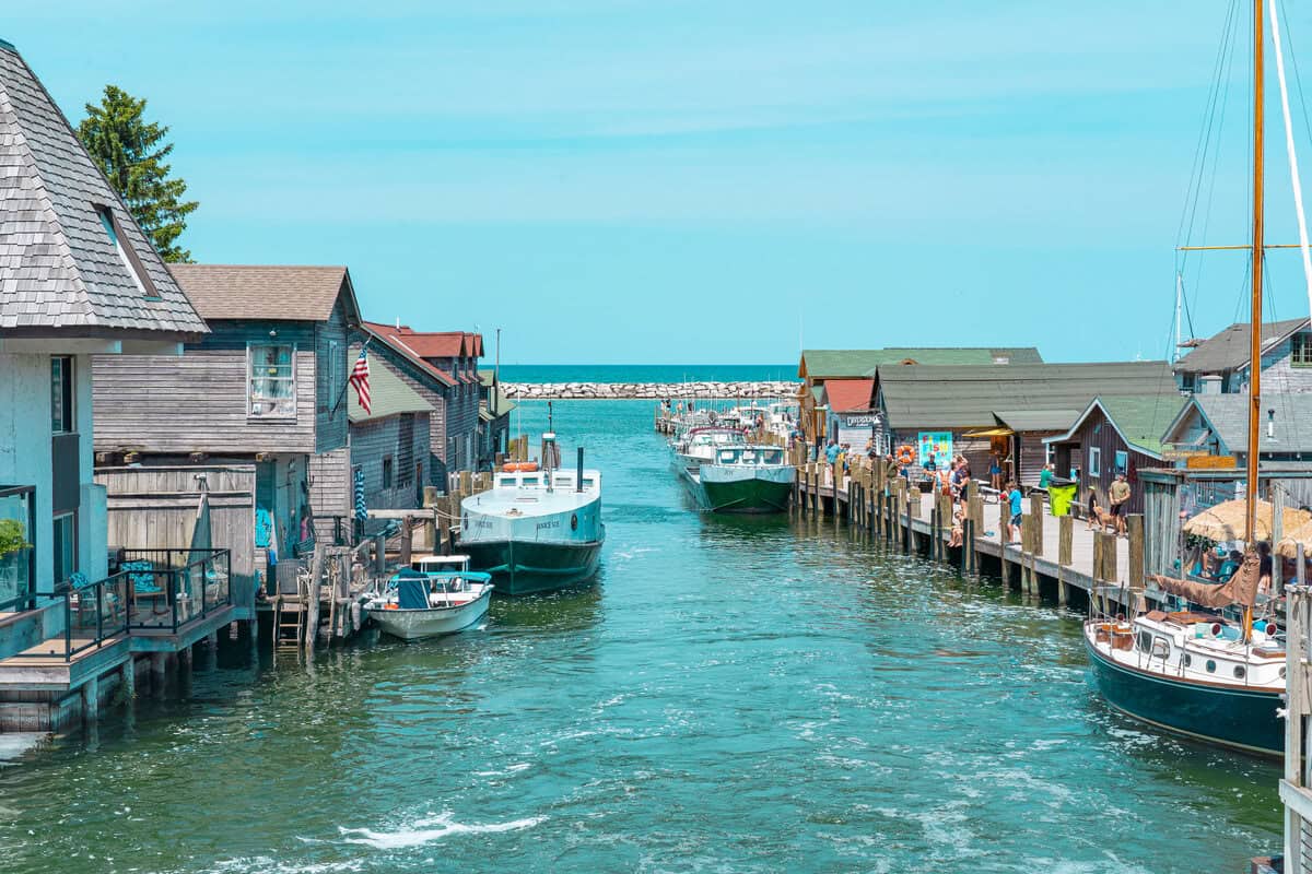 A canal between wooden waterfront buildings with boats and people enjoying a sunny day.