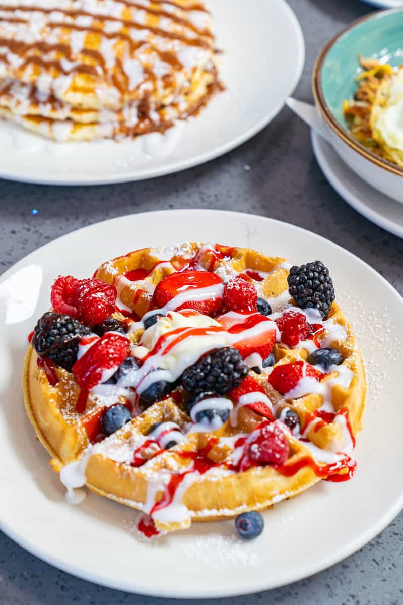 A waffle topped with berries, cream, and syrup on a white plate