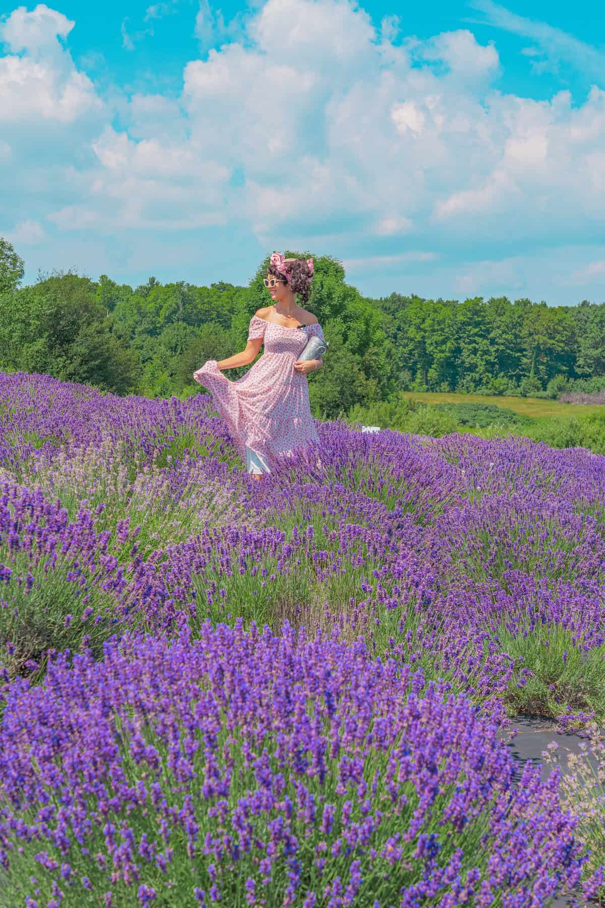 Person in a pink dress holding skirt amidst a field of lavender blooms under a blue sky.