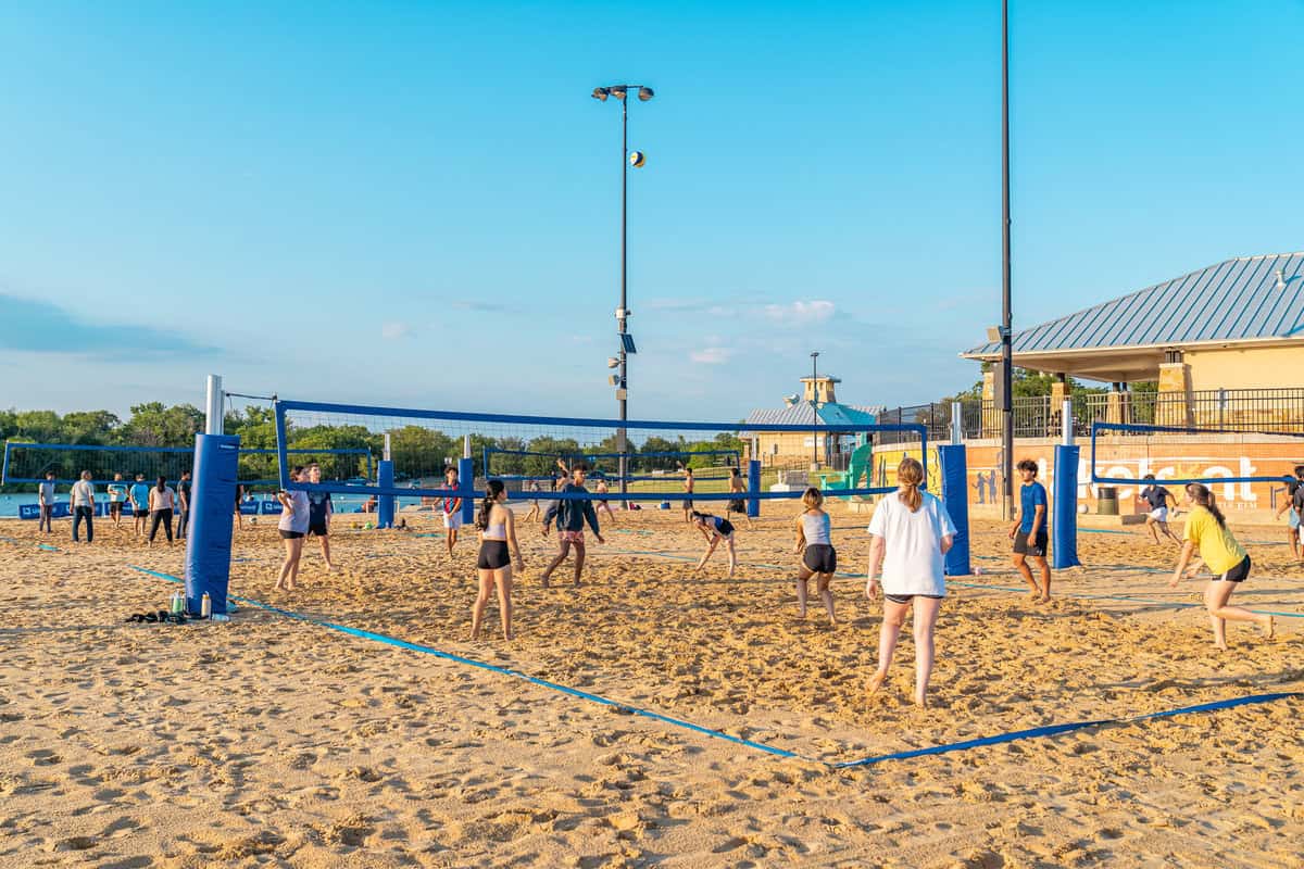 People playing volleyball on an outdoor sand court at dusk.