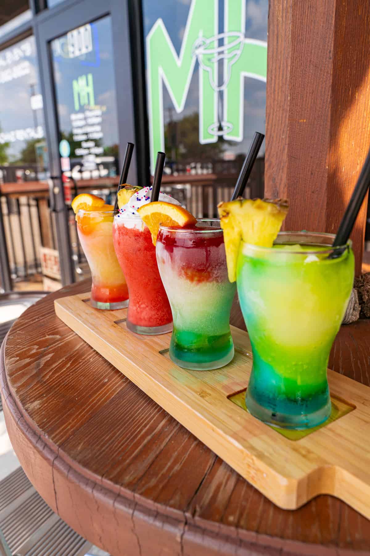 Three colorful frozen cocktails on a wooden tray