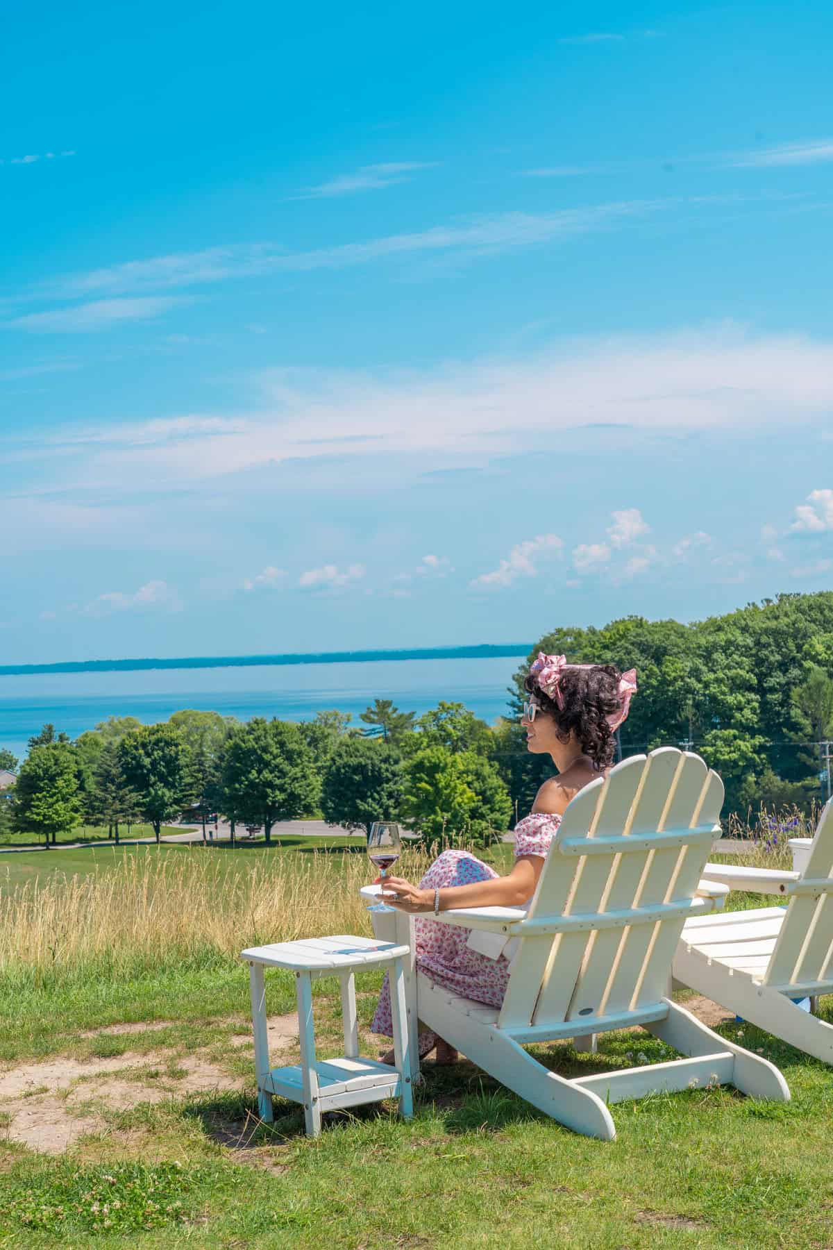 Person in a pink dress sitting on an Adirondack chair by the sea