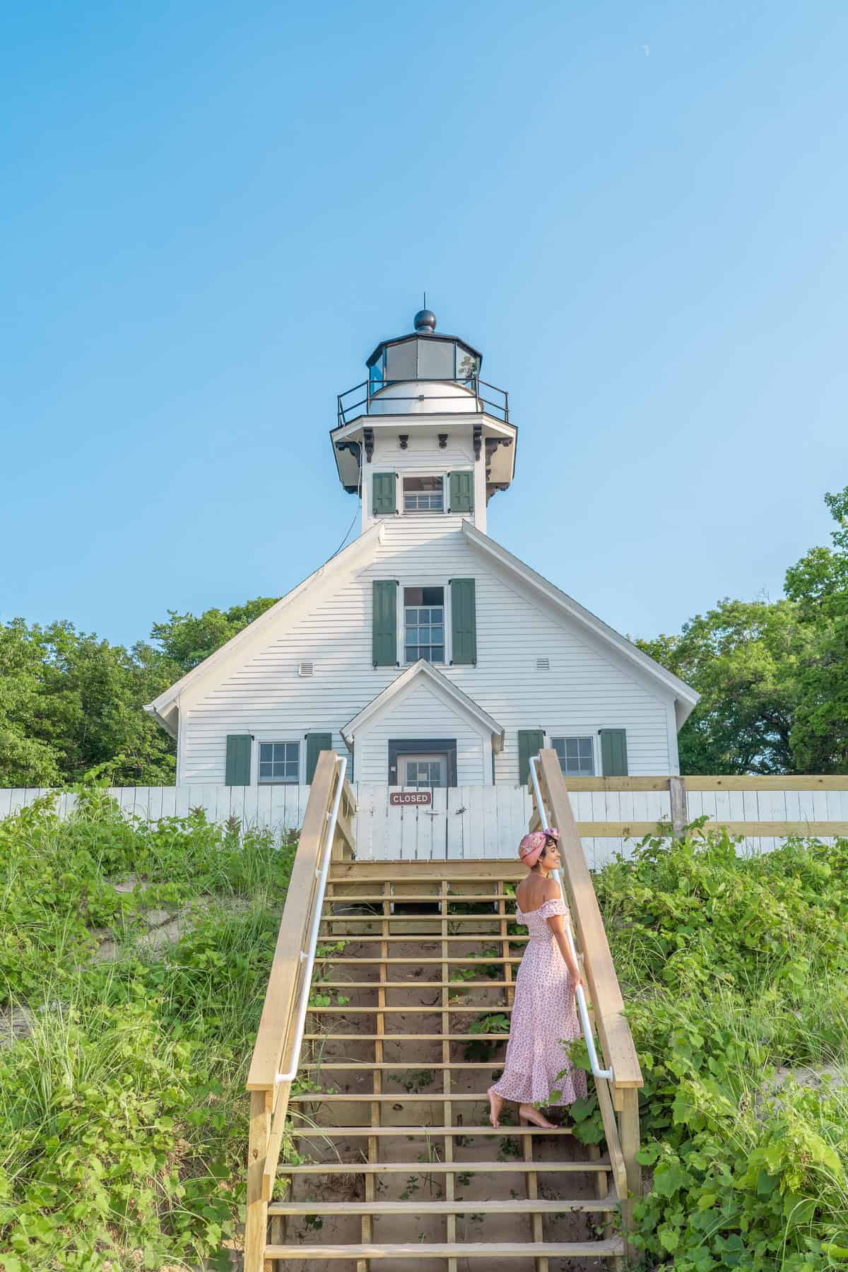 Person in pink dress on stairs leading to a white lighthouse with "CLOSED" sign.