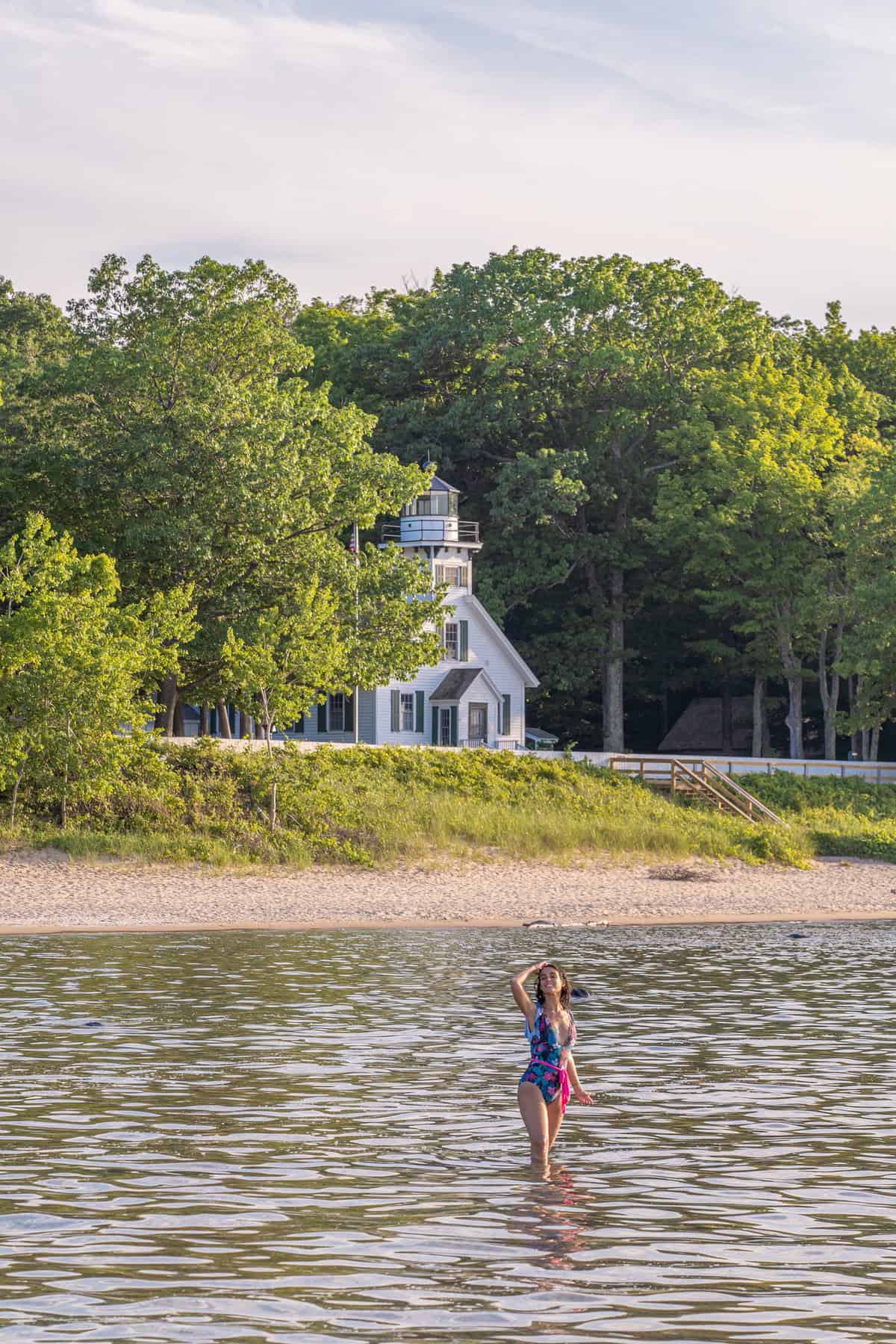 Person standing in water near a beach with a lighthouse