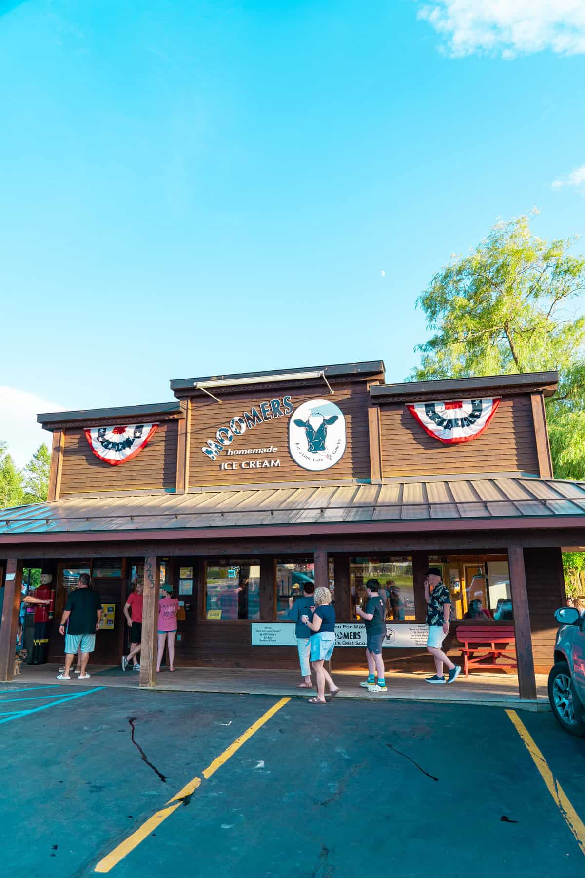 People outside an ice cream shop with patriotic decorations under a clear sky.