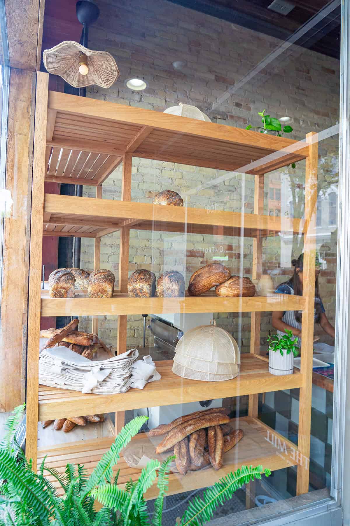 A bakery window display featuring shelves of fresh bread against a brick wall background.