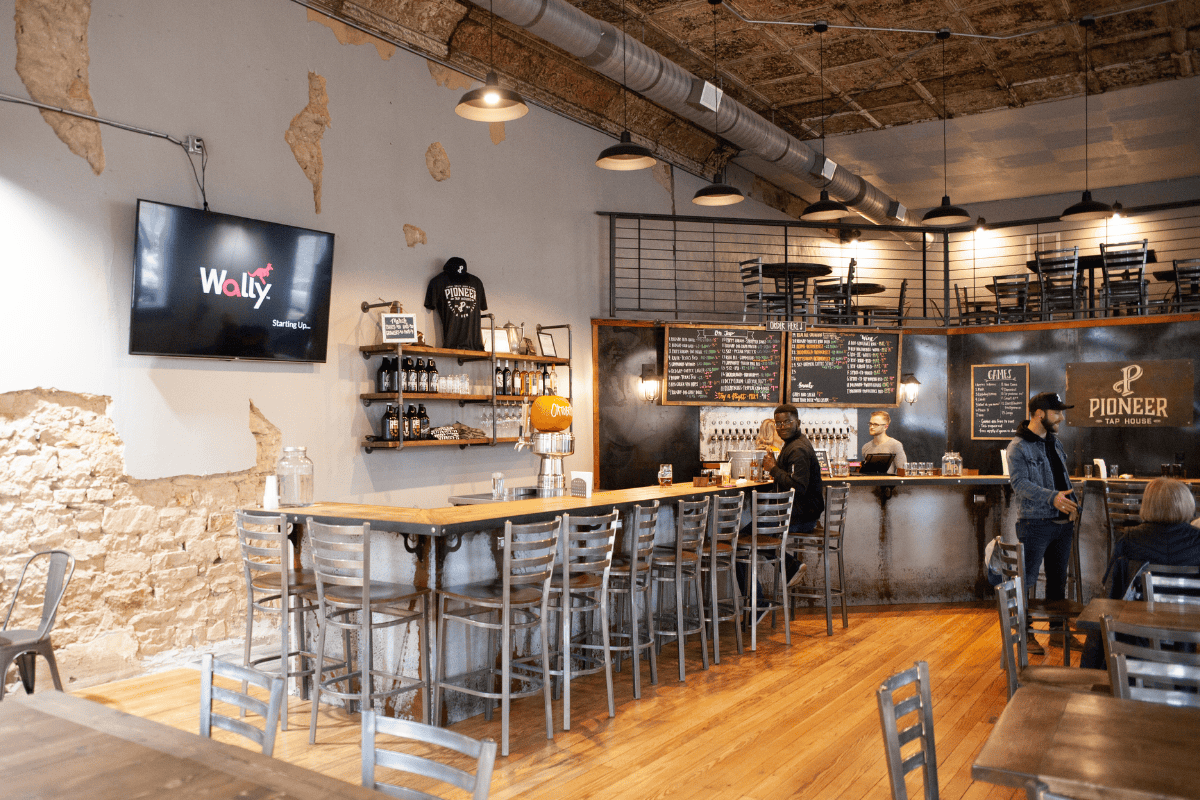 Rustic tap house with wooden tables, metal chairs, and a bar with menu boards.