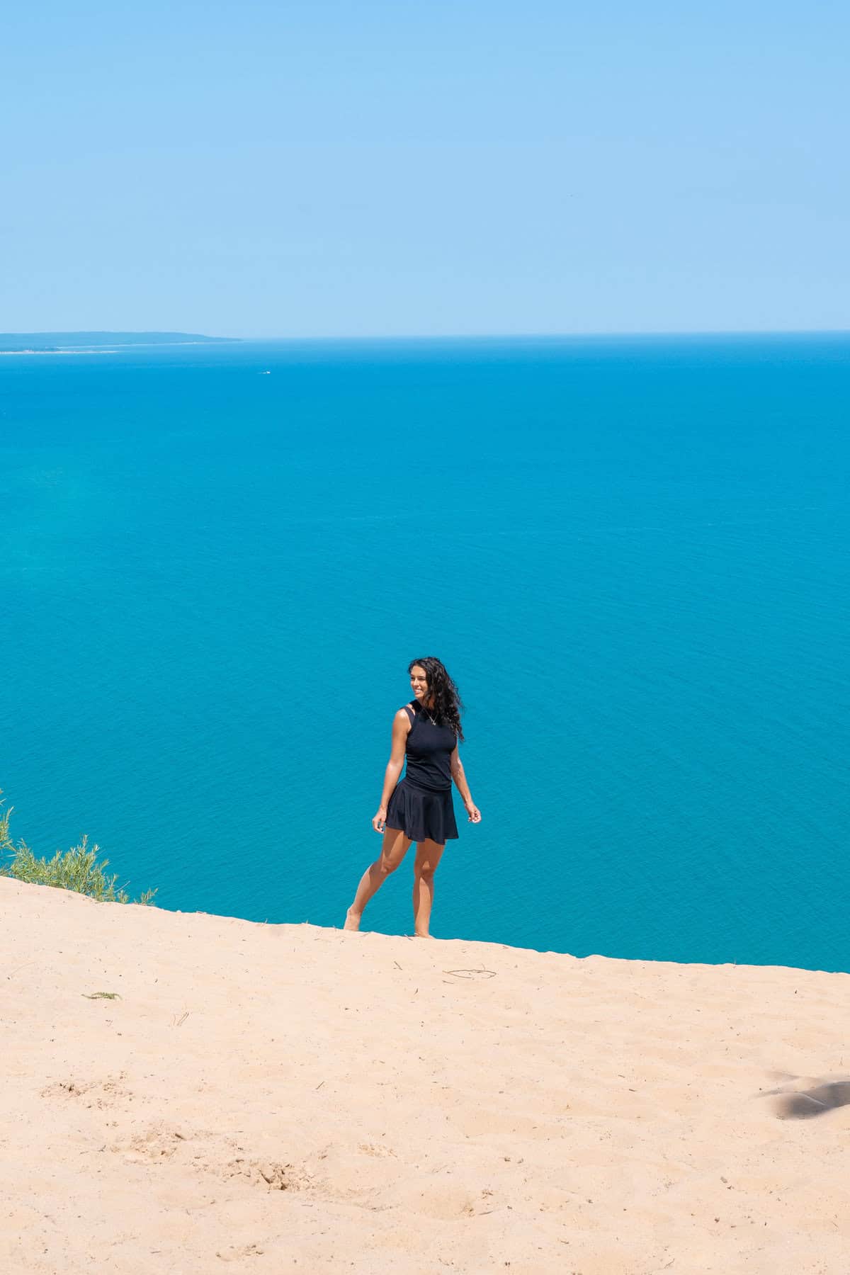 Person standing on a sandy cliff overlooking a calm blue sea.