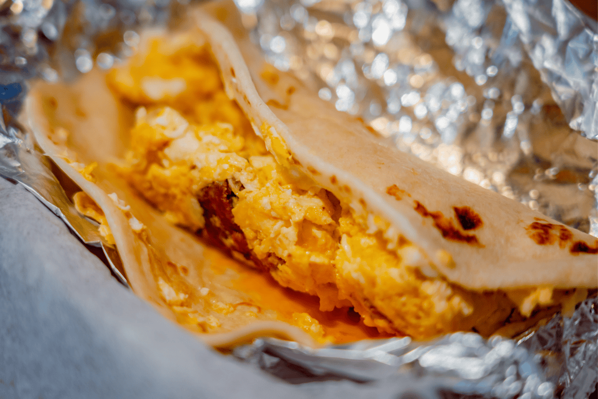 Breakfast burrito with eggs and cheese on foil.