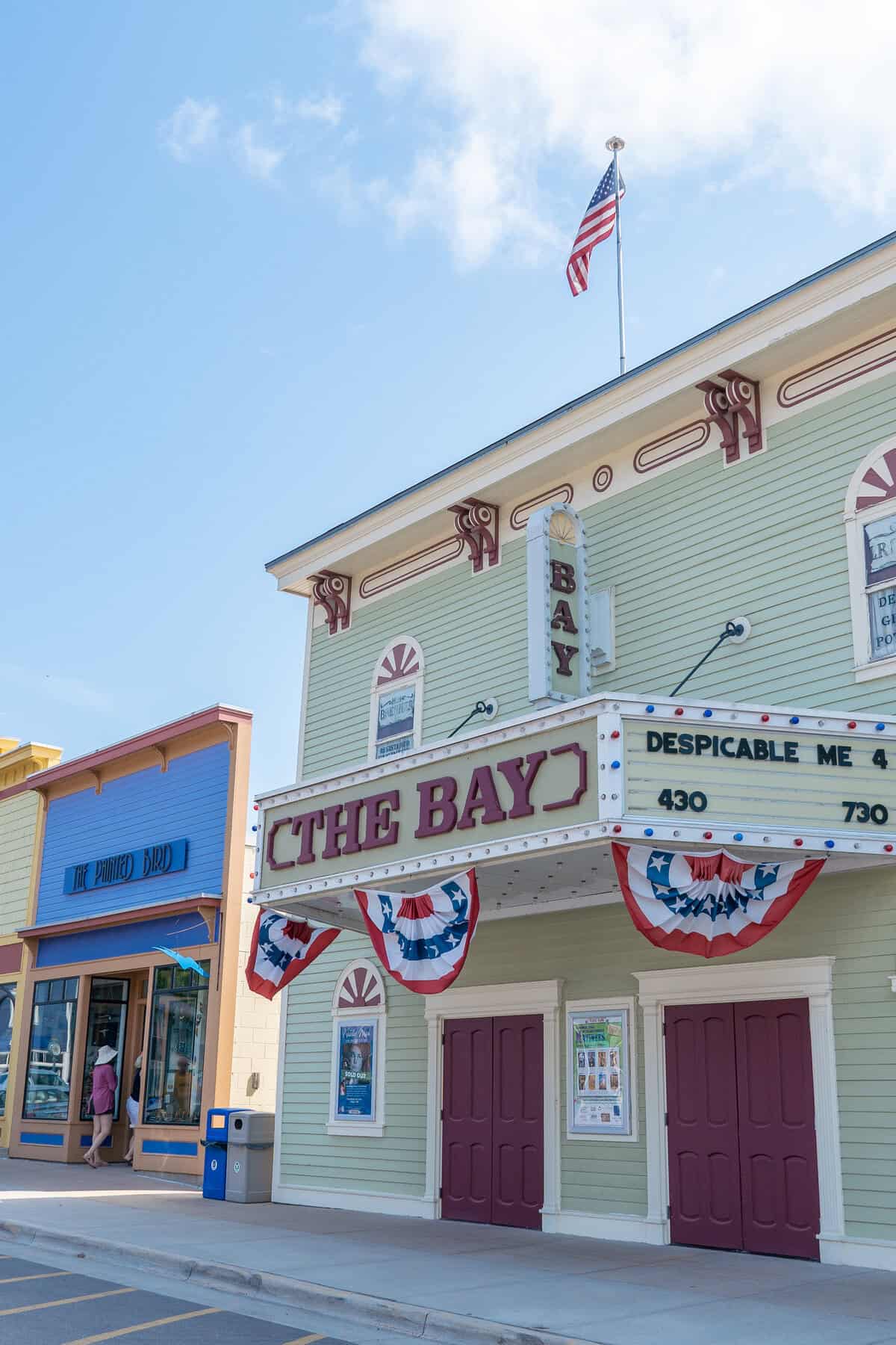 Exterior of "THE BAY" theater with patriotic banners, under a blue sky with an American flag atop.