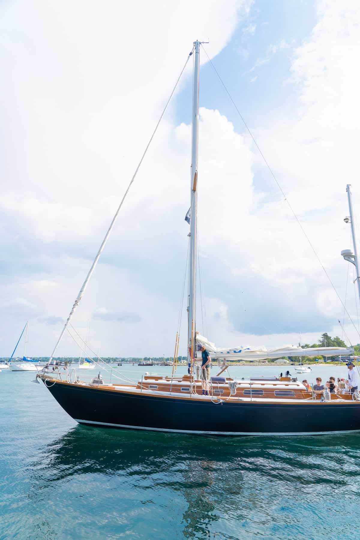 A large sailboat with people on deck moored in a calm bay under a blue sky.