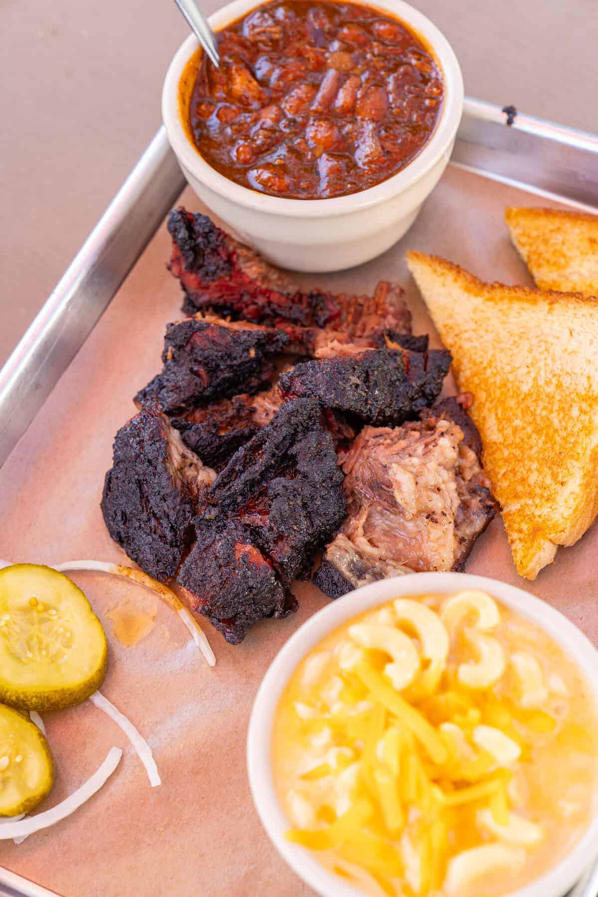 A plate with burnt ends, toast, pickles, macaroni and cheese