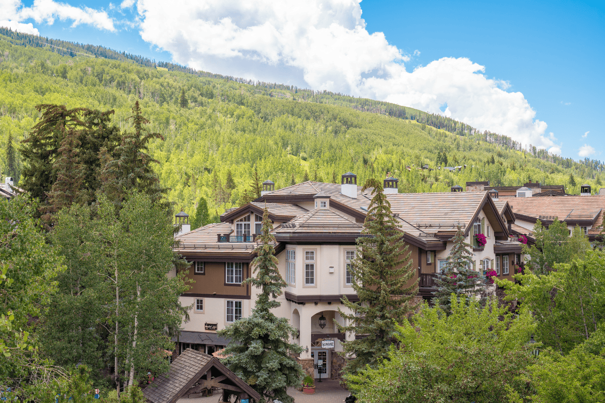 Alpine-style building nestled in lush greenery with mountain backdrop.