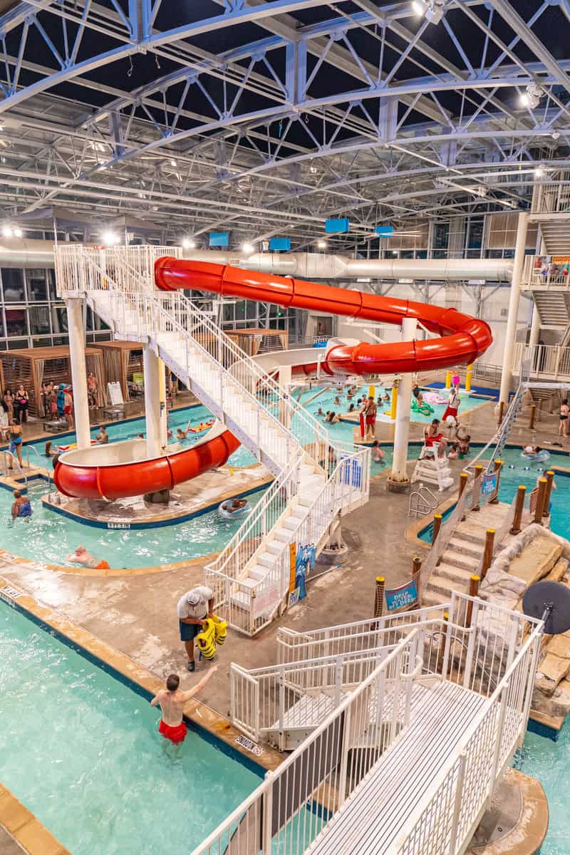 Indoor water park with a red slide, pools, and visitors enjoying various activities.