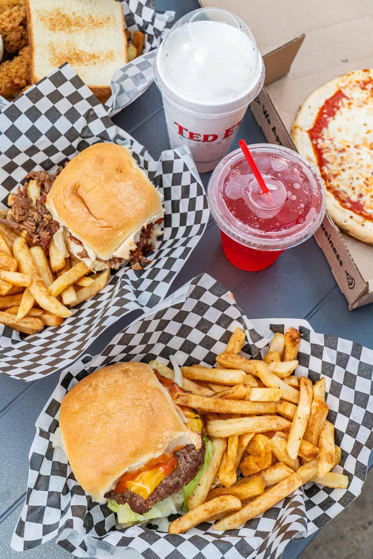 Fast food meal with burgers, fries, chicken tenders, pizza, and drinks.