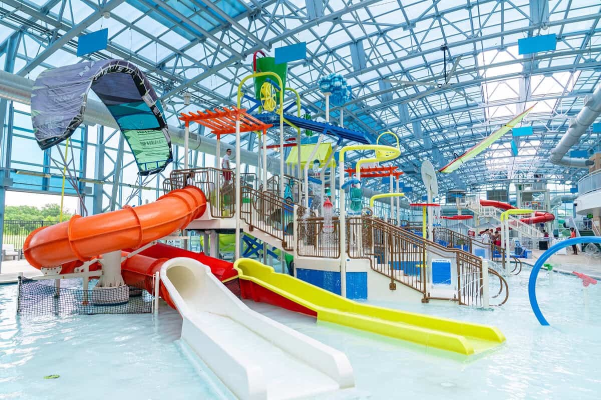 Indoor water park with a play structures under a blue glass ceiling.