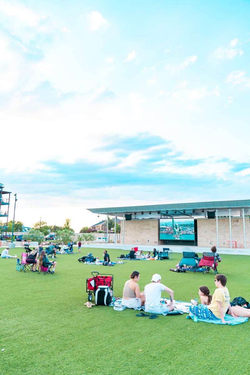 People relaxing on a lawn in front of a stage on a sunny day.