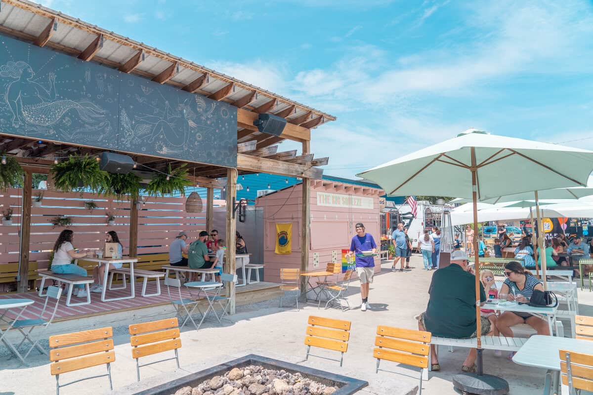 Outdoor food market with patrons dining under umbrellas on a sunny day.