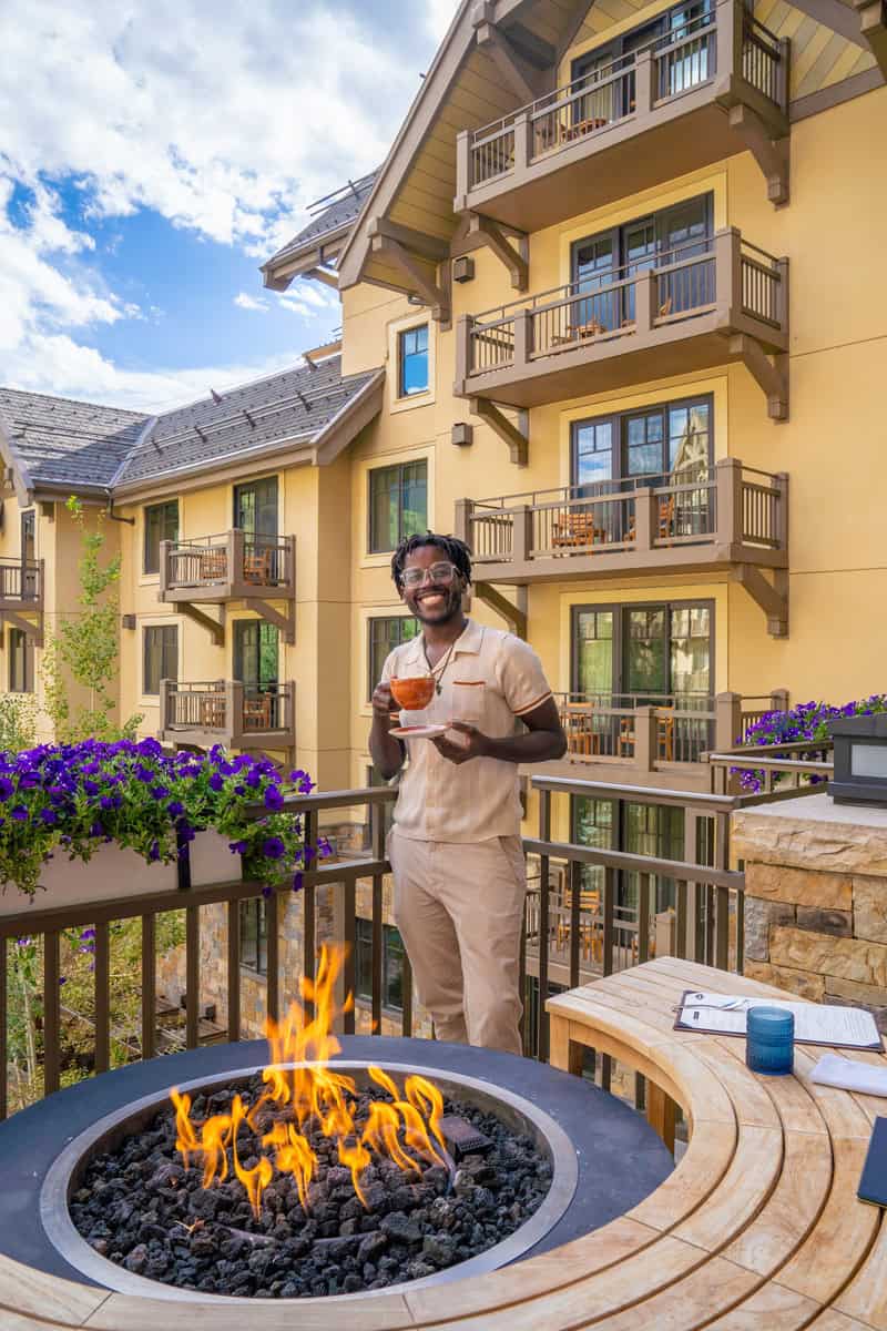 Person holding a drink by a fire pit on a balcony