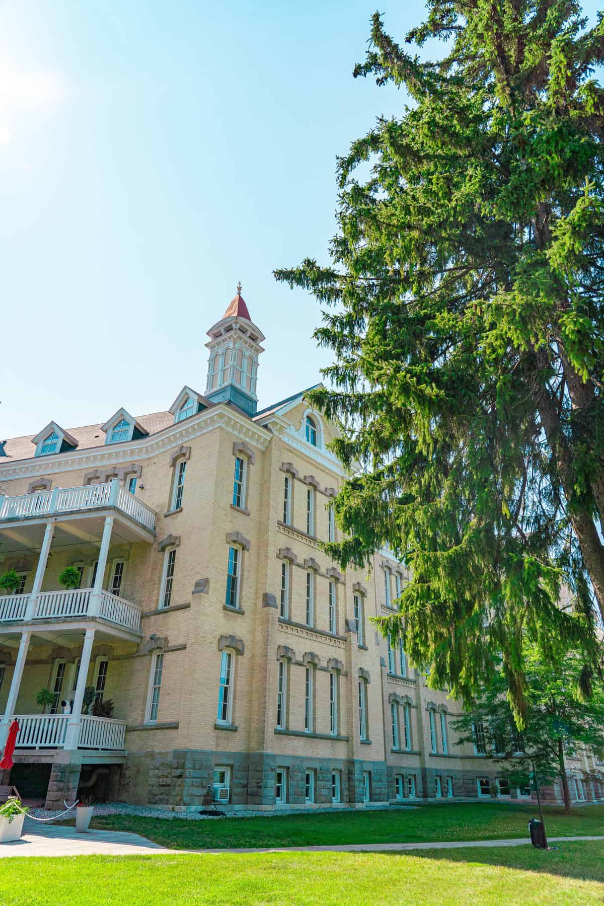 Historic building with a tower and balcony surrounded by trees under a blue sky.