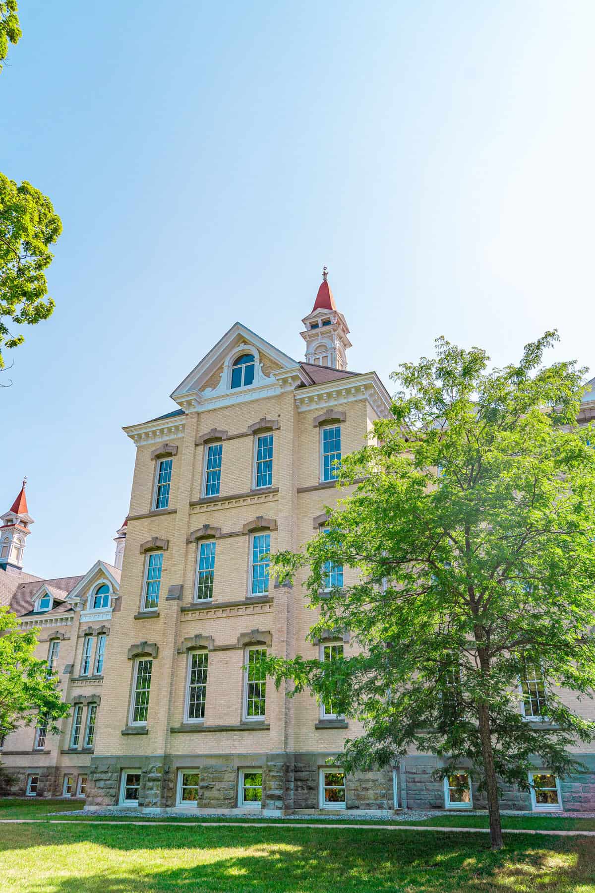 Historic brick building with a red spire, surrounded by green trees against a blue sky.