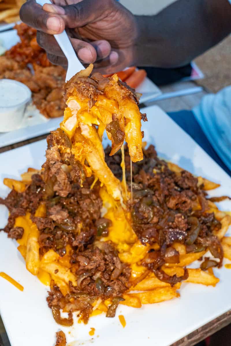 A person lifting a forkful of cheesy fries topped with chili.