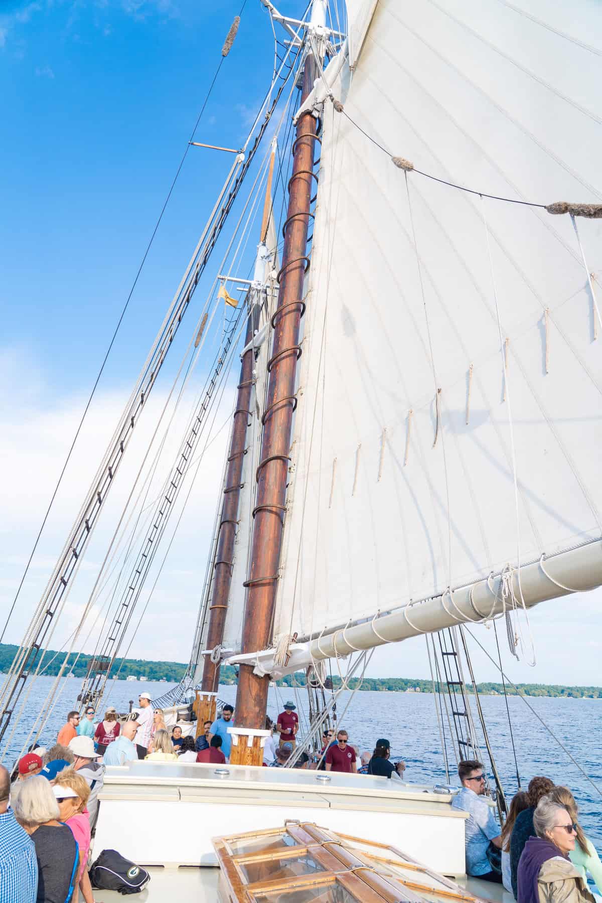 Passengers on a sailboat with a white sail against a blue sky.