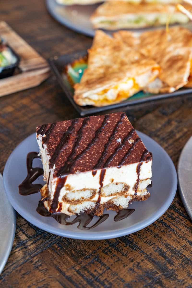 Slice of tiramisu with chocolate drizzle on a gray plate