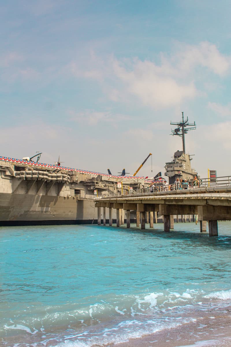 Aircraft carrier museum on a sunny day viewed from the beach with clear blue water.