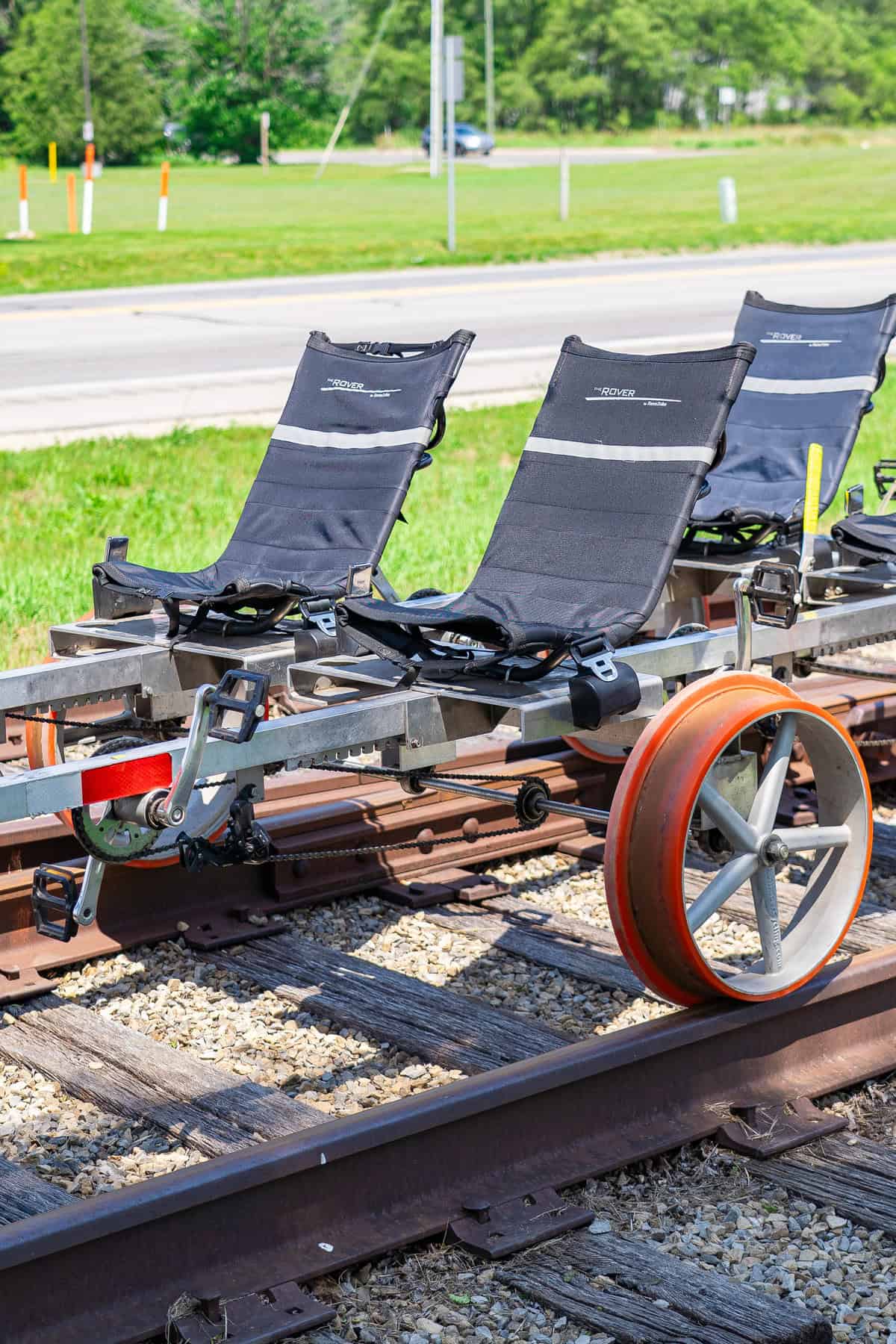 Railroad pedal trolley with three seats on tracks, outdoors.