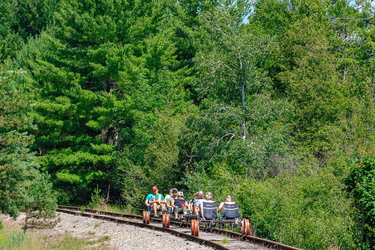 People riding pedal-powered rail bikes through a wooded area.