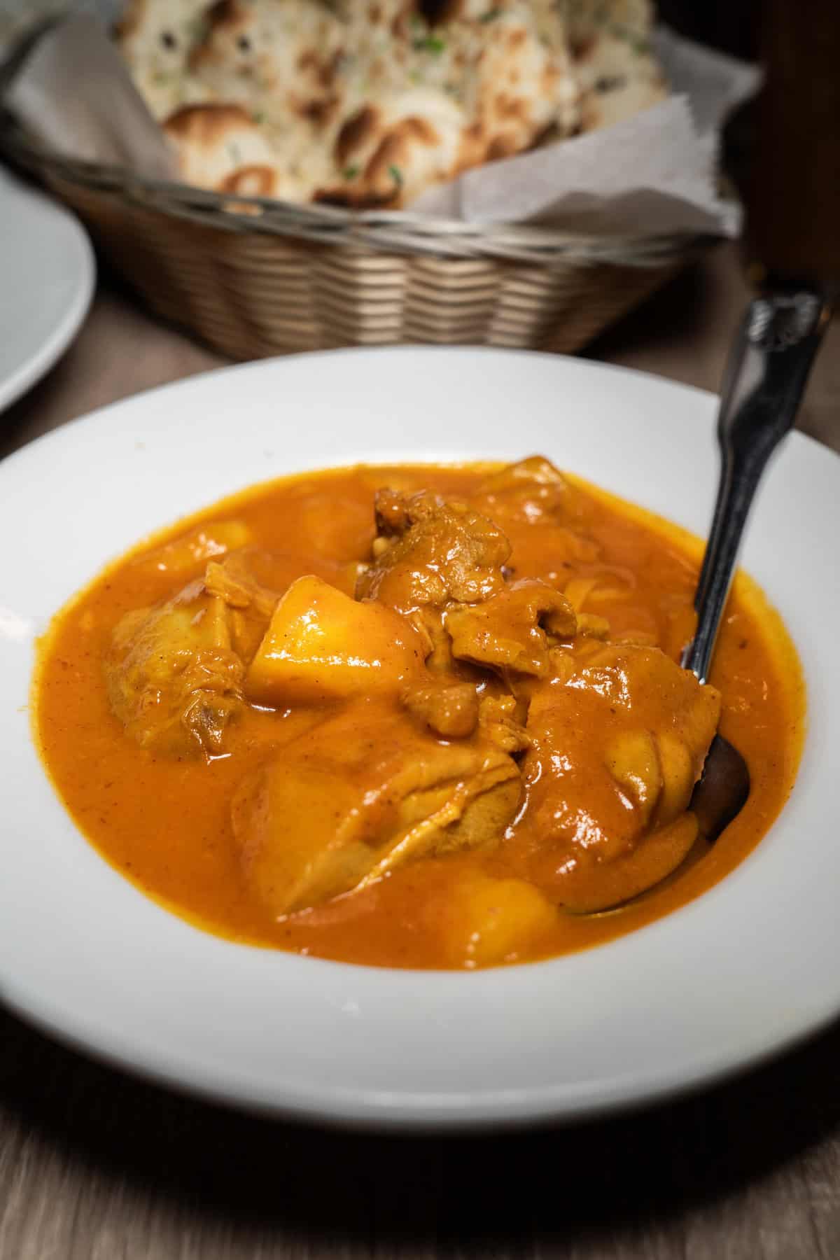 A bowl of chicken curry with bread in the background.