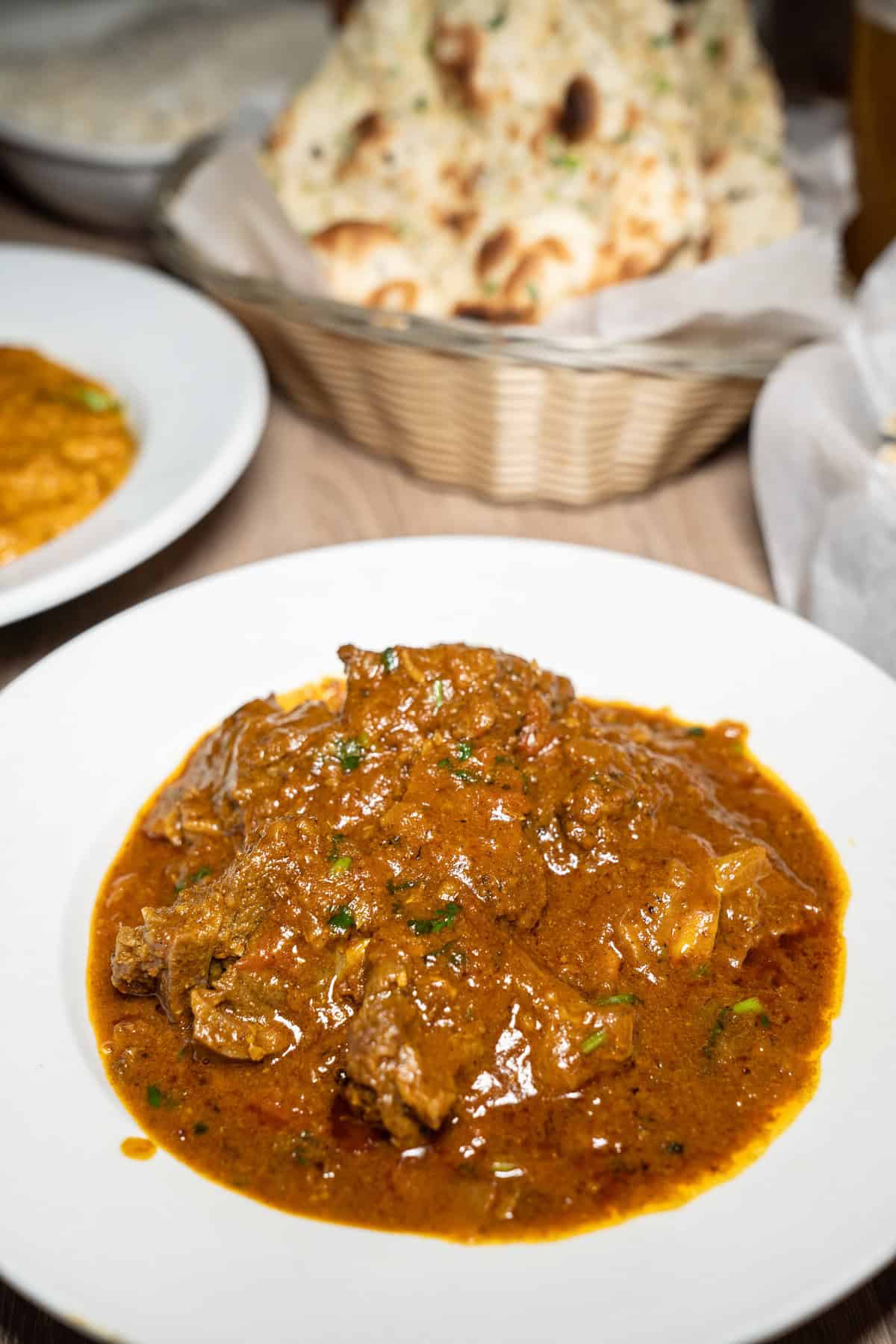 A plate of rich, spicy curry with naan in the background.