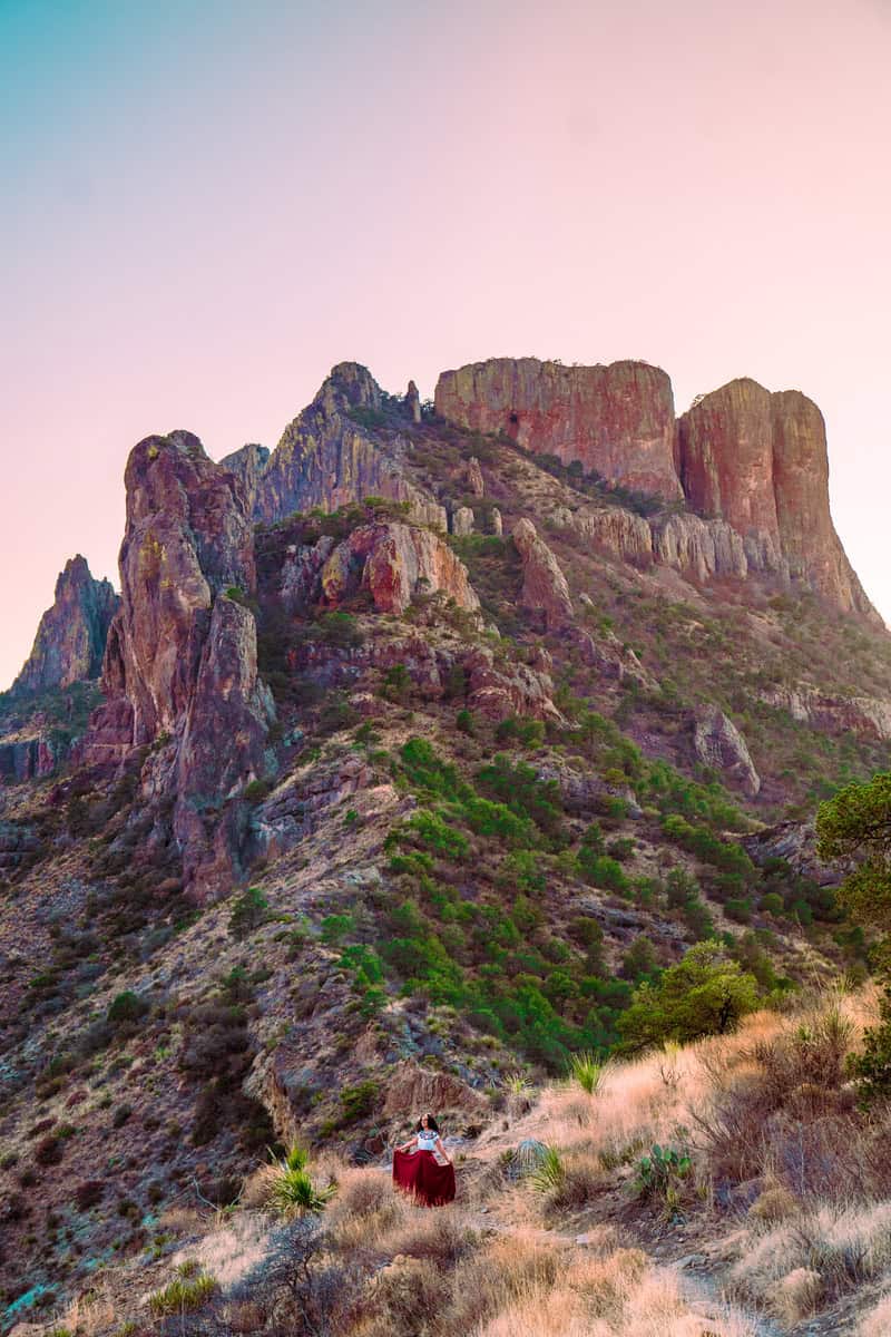 Person in red sitting below rocky cliffs at sunset.