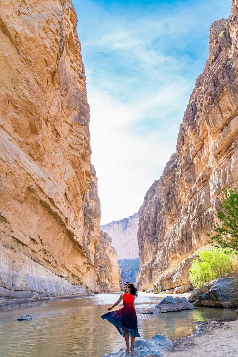 A person in a red top and blue skirt standing by water in a canyon