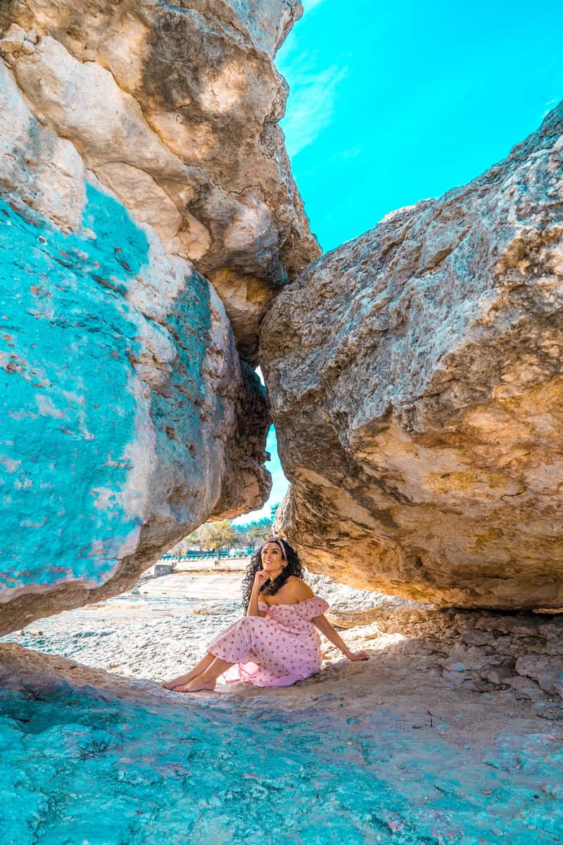 Person in a pink dress sitting between large rocks