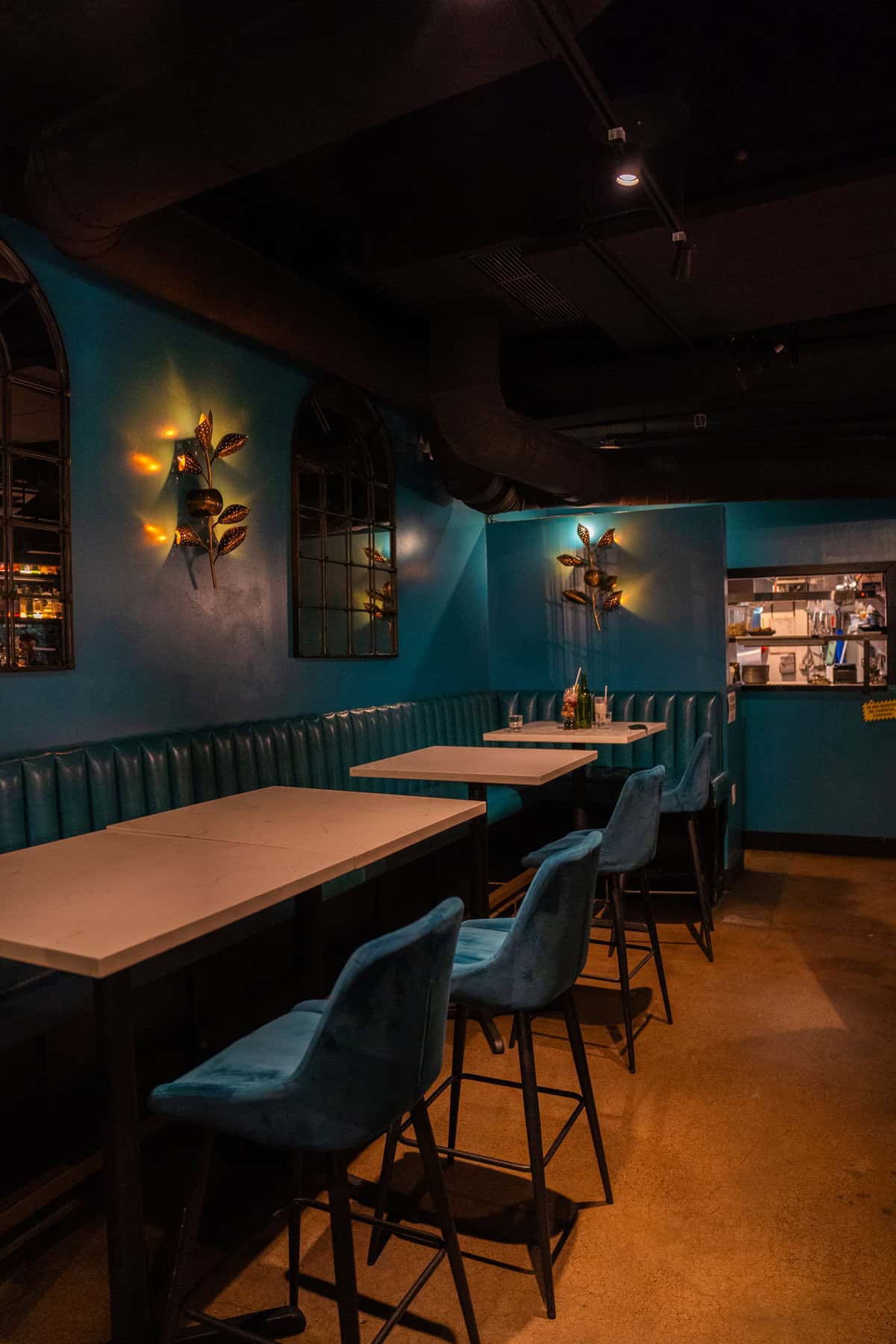 Dimly lit bar with teal walls, booth seating, and decorative