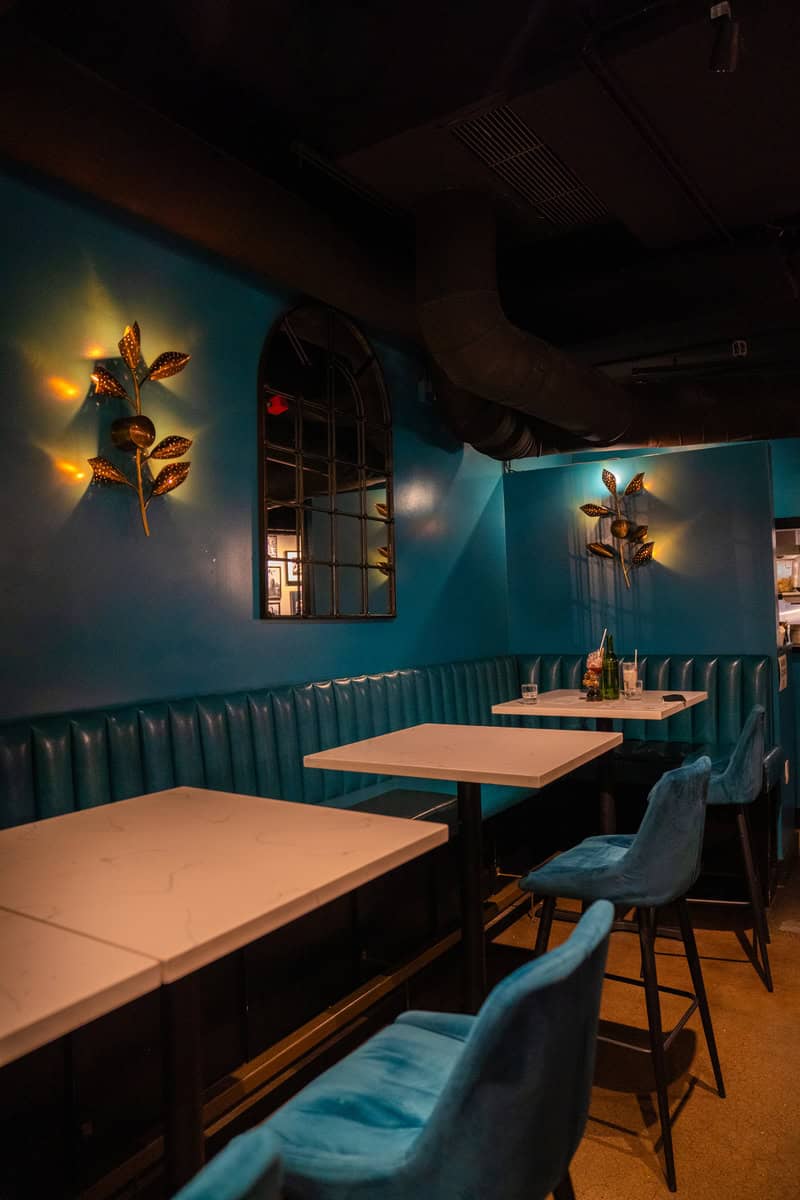 Dimly lit bar with teal booths, white tables, and decorative wall lights.