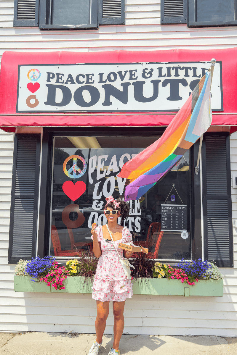 Person in a floral dress holding a donut box outside a shop