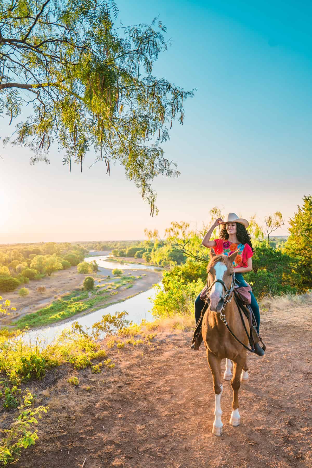 Person on a horse on a scenic trail near a river with lush greenery.