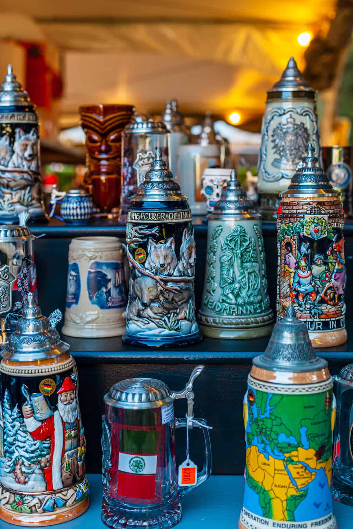 Decorative beer steins and a glass teapot displayed on a shelf.